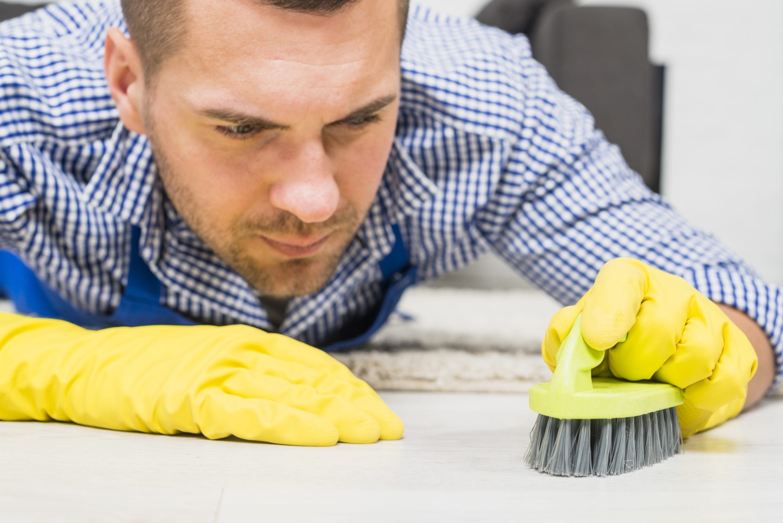 Gloved hand scrubbing a hard floor with a brush