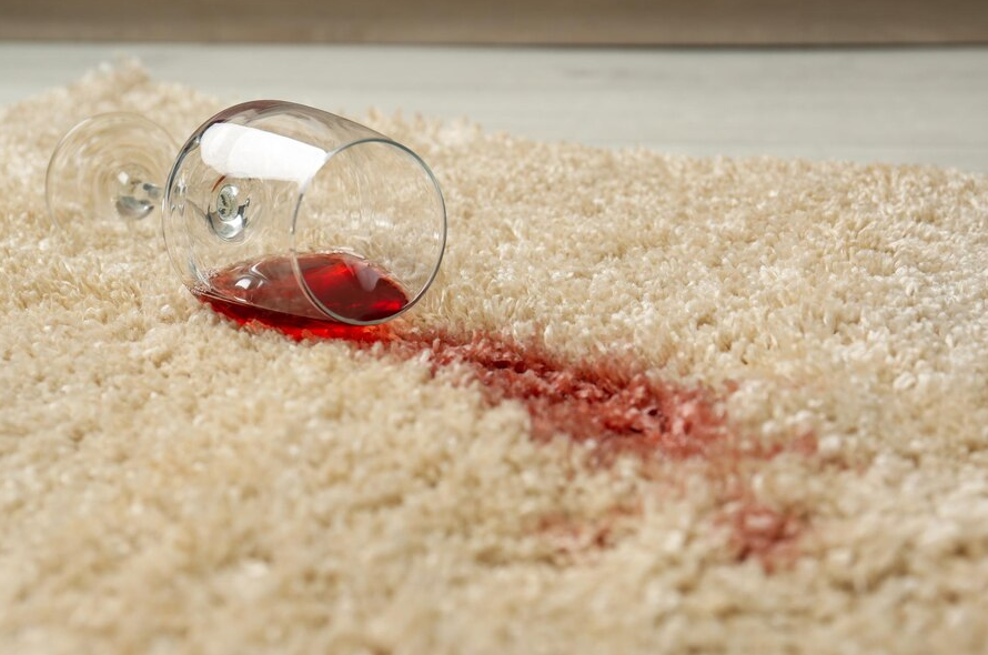 Overturned wine glass spilling red wine on a cream rug