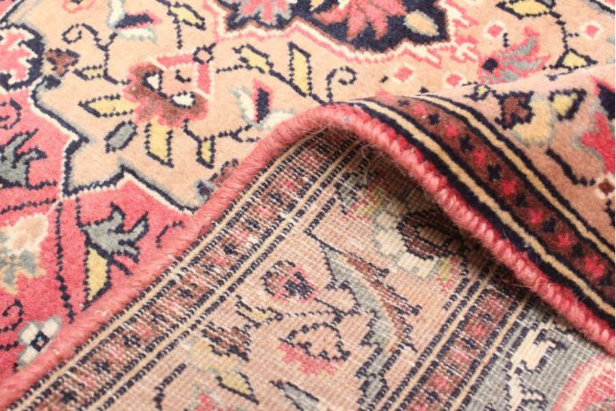 Folded corner of a pink and tan floral rug