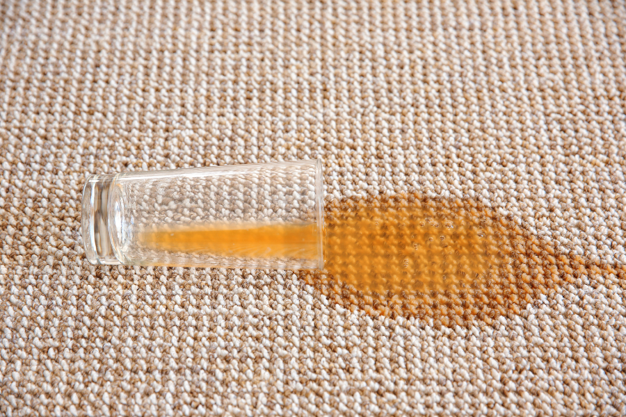 Overturned glass spilling amber liquid on a woven carpet