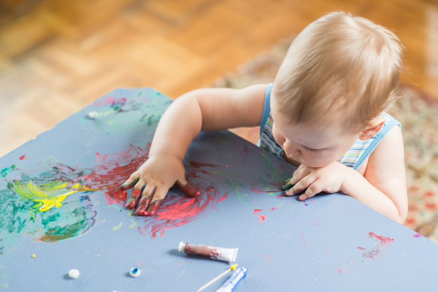 Baby fingerpainting at a table with a rug on the floor behind