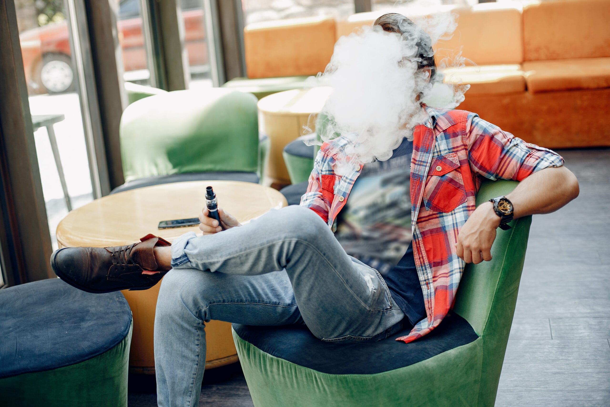 Man exhaling vape smoke while seated in a lounge chair