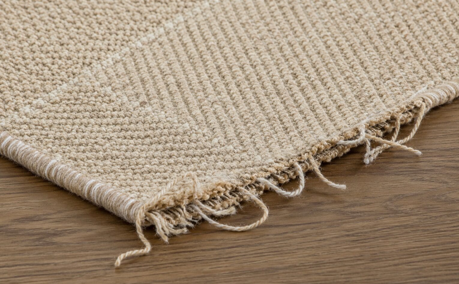 Tan woven rug corner with a frayed fringe