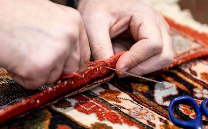 Hands hand-stitching binding onto a rug border