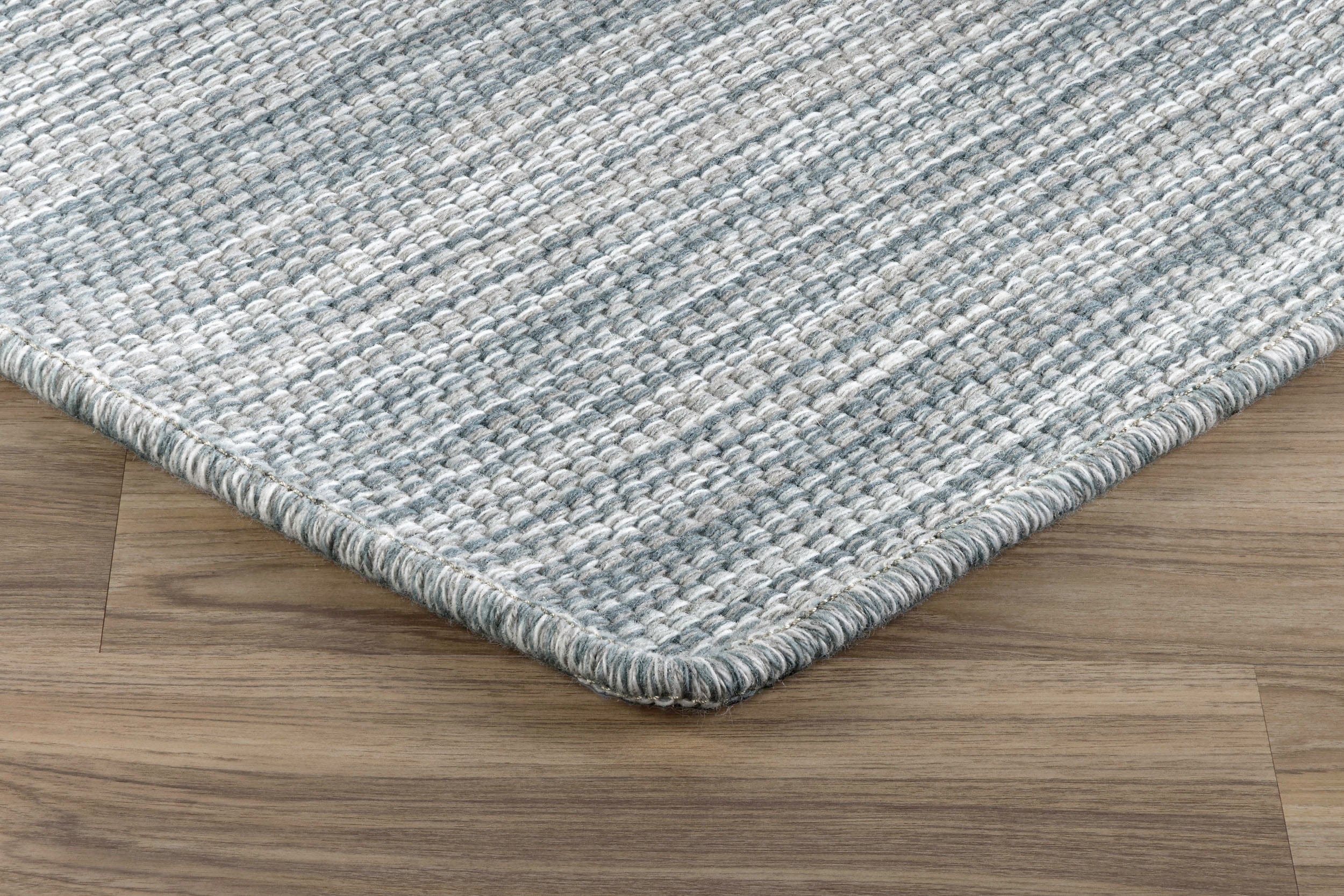 Grey woven rug corner with a serged edge