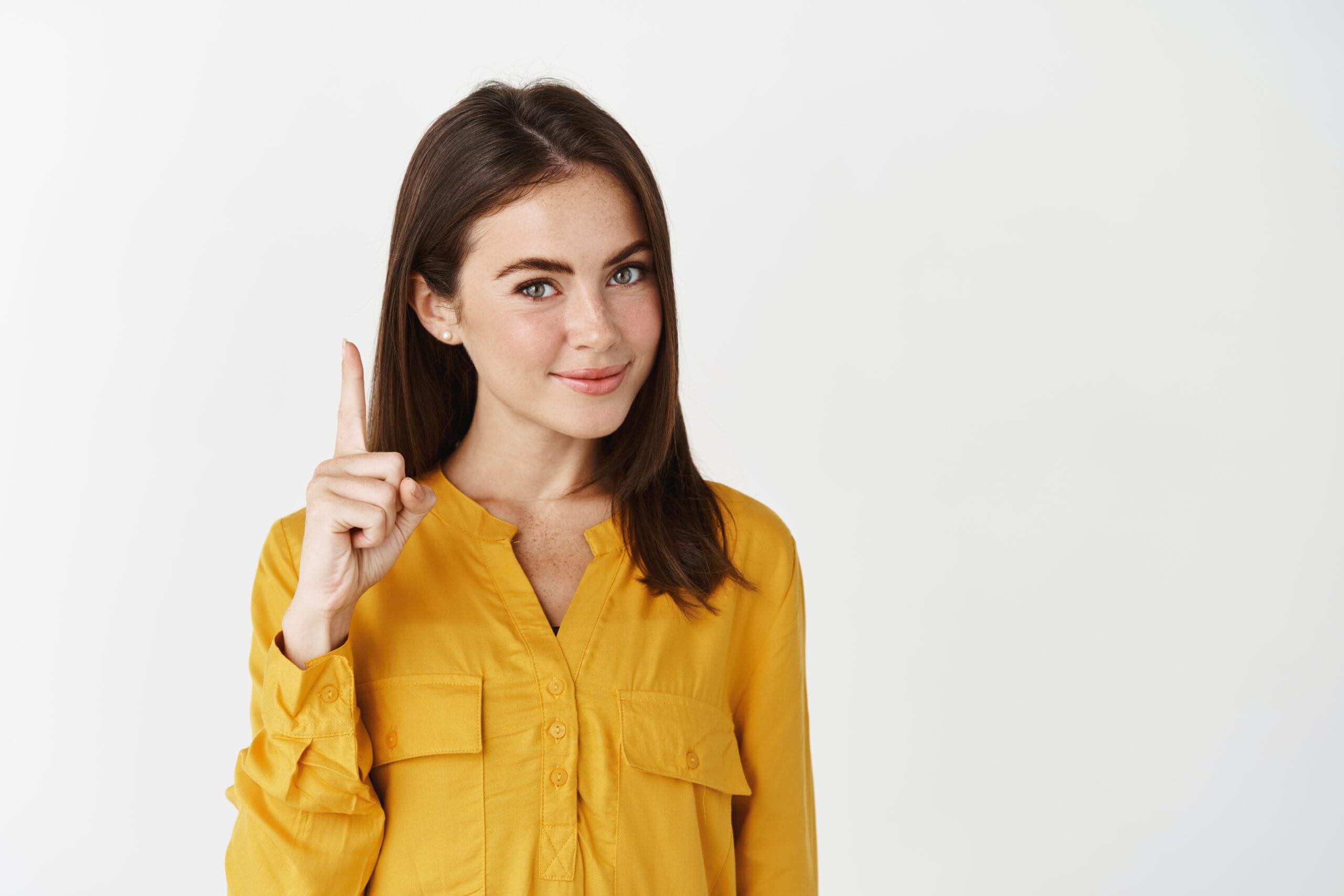 Woman in a yellow blouse pointing up with one finger