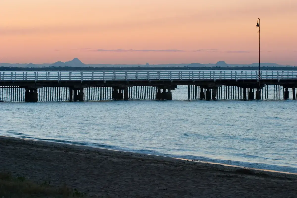 Shorncliffe pier at dusk with the Glass House Mountains on the horizon